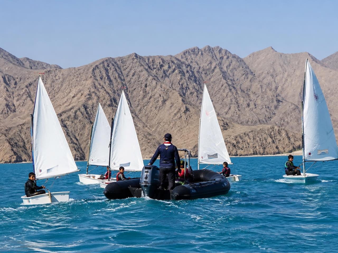 Children and a coach training in dinghies on warm turquoise water in Oman
